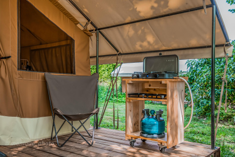 Terrazza della tenda safari con sedia, fornello a gas e bombola verde presso Onlycamp Camping Le Lac de Roybon, Francia.
