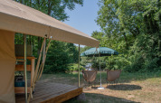 Tenda safari con terrazza in legno, sedie da campeggio e ombrellone presso Camping Le Lac de Roybon, Francia.