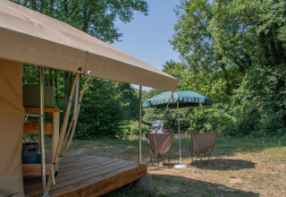 Tenda safari con terrazza in legno, sedie da campeggio e ombrellone presso Camping Le Lac de Roybon, Francia.