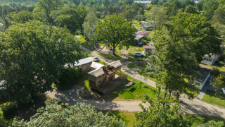 Luchtbeeld van een boomhuttent met bubbelbad, omringd door bomen en huisjes in een groene omgeving.