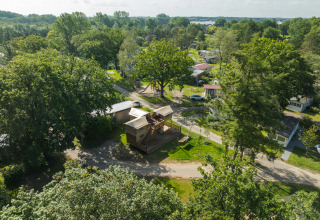 Luchtfoto van een boomhuttent met bubbelbad, omgeven door bomen en huisjes op een groen, bosrijk terrein.