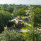 Luchtfoto van een boomhuttent met bubbelbad, omgeven door bomen en huisjes op een groen, bosrijk terrein.