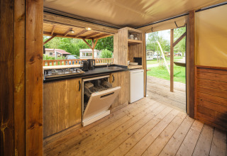 Buitenkeuken met houten vloer, open vaatwasser en uitzicht op kampeerterrein bij Holiday park Mölke.