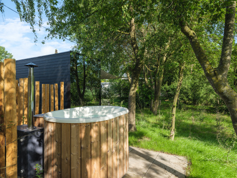 Buiten hottub bij River Mirrorlodge in Holiday park Mölke, Nederland, omgeven door groene bomen.