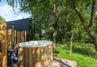 Buiten hottub bij River Mirrorlodge in Holiday park Mölke, Nederland, omgeven door groene bomen.