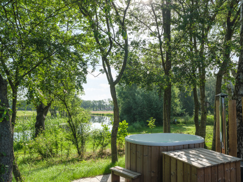 Houten hottub bij River Mirrorlodge in Holiday park Mölke, met uitzicht op bomen en rivier in Nederland.
