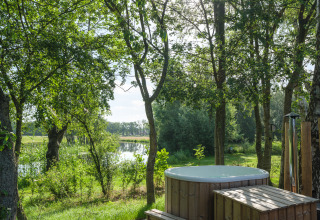 Houten hottub bij River Mirrorlodge in Holiday park Mölke, met uitzicht op bomen en rivier in Nederland.
