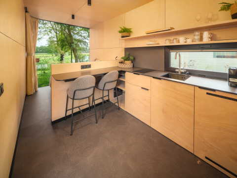 Moderne lodgekeuken met barstoelen, grote ramen en uitzicht op natuur bij Holiday park Mölke.