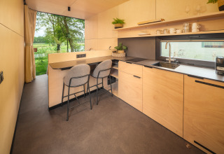 Moderne lodgekeuken met barstoelen, grote ramen en uitzicht op natuur bij Holiday park Mölke.