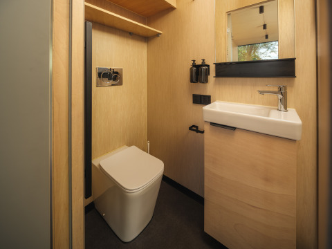 Moderne badkamer met houten wanden, vierkante wc en wastafel in River Mirrorlodge, vakantiepark Mölke, Nederland.