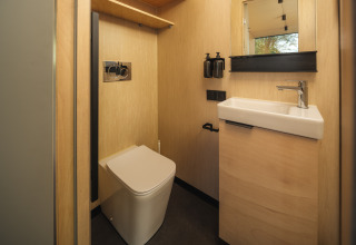 Moderne badkamer met houten wanden, vierkante wc en wastafel in River Mirrorlodge, vakantiepark Mölke, Nederland.