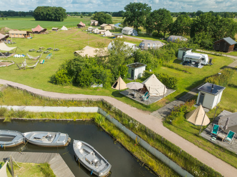 Luftfoto af Blije haventent tipi med private sanitetsfaciliteter, både og telte på en grøn campingplads.