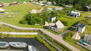 Luchtfoto van Blije haventent tipi met eigen sanitair, boten en tenten op een groene campinglocatie.