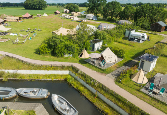 Luftfoto af Blije haventent tipi med private sanitetsfaciliteter, både og telte på en grøn campingplads.