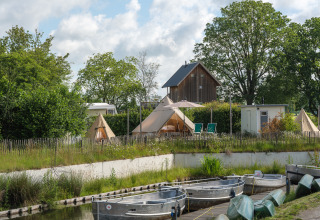 Udsigt over både og teepee-telte ved «Blije haventent» på ferieparken Mölke, Holland, omgivet af grønne træer.
