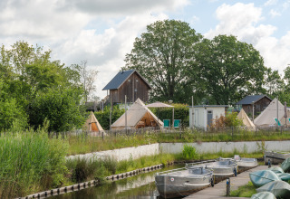 Tipi-tenten bij vakantiepark Mölke in Nederland, met bootjes aan een kanaal en groene bomen eromheen.