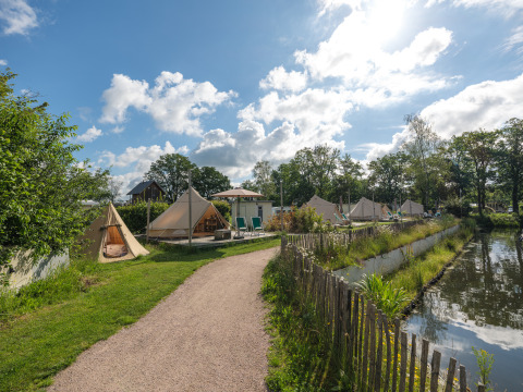 Teepee-telte ved vandets kant på Holiday park Mölke i Holland, med grønne omgivelser og blå himmel.