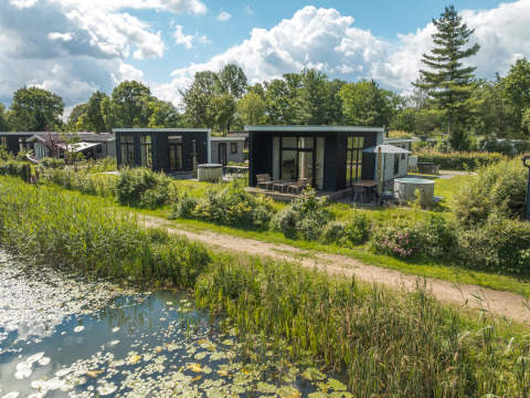 Foto van River Cabin lodge met hot tub, gelegen aan een vijver en omringd door groene natuur.