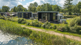 Foto einer River Cabin Lodge mit Whirlpool, neben einem Teich und inmitten von grüner Natur gelegen.
