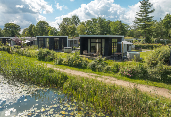 Foto van River Cabin lodge met hot tub, gelegen aan een vijver en omringd door groene natuur.