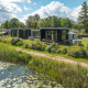 Billede af River Cabin lodge med hot tub ved siden af en sø, omgivet af grønne planter og natur.
