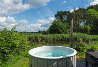 Udendørs badekar på River Cabin ved Holiday park Mölke i Holland, med naturudsigt og blå himmel.