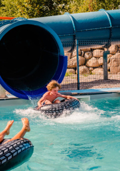 Children enjoy a water slide at Camping La Sténiole in Grand Est, France, with an adult supervising in the pool.