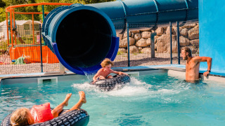 Children enjoy a water slide at Camping La Sténiole in Grand Est, France, with an adult supervising in the pool.