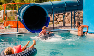 Children enjoy a water slide at Camping La Sténiole in Grand Est, France, with an adult supervising in the pool.