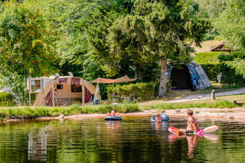 Camping La Sténiole dans le Grand Est, France, avec familles jouant dans le lac et tentes près de l'eau.