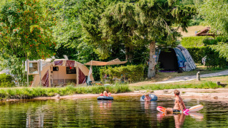 Camping La Sténiole in Grand Est, France, with families playing in the lake and tents set up by the water.