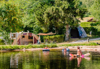 Camping La Sténiole in Grand Est, Frankrijk, met spelende families in het water en tenten bij het meer.
