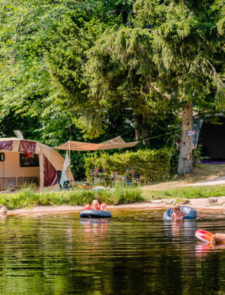 Camping La Sténiole in Grand Est, France, with families playing in the lake and tents set up by the water.