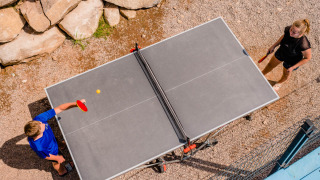 Two people play outdoor table tennis at Camping La Sténiole, a holiday park in Grand Est, France.