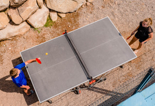 Two people play outdoor table tennis at Camping La Sténiole, a holiday park in Grand Est, France.