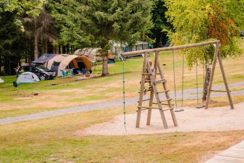 Vakantiepark met tenten, wagens en kinderen op een houten speeltuin in het bosrijke Grand Est, Frankrijk.