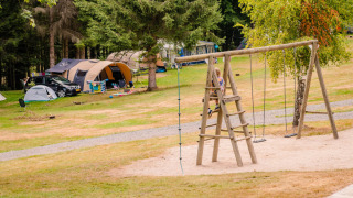 Campsite with tents, cars, and children playing on a wooden playground in a forested area in Grand Est, France.