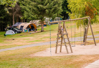 Terrain de camping avec tentes, voitures et enfants jouant sur une aire de jeux en bois à Grand Est, France.