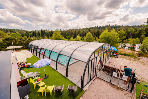 Piscine couverte entourée de chaises longues et de nature au Camping La Sténiole en Grand Est, France.