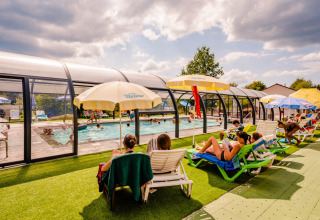 Gæster slapper af ved en overdækket swimmingpool på Camping La Sténiole feriepark i Grand Est, Frankrig.