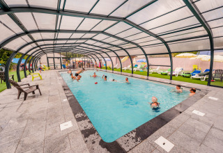 Piscina coperta con persone che nuotano e giocano al Camping La Sténiole in Grand Est, Francia.