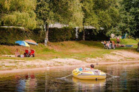 Persone si rilassano a riva e remano su un gommone al Camping La Sténiole, Grand Est, Francia.