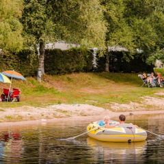 People relax on the shore and paddle in an inflatable boat at Camping La Sténiole, Grand Est, France.