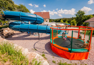 Spielplatz mit großer blauer Rutsche und rundem Trampolin im Camping La Sténiole, Grand Est, Frankreich.