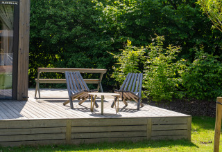 Terrazza in legno con sedie e tavolo al Tiny Home Urban-Gardens Gent in Belgio, circondata dal verde.
