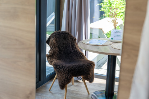 Coin accueillant dans une Tiny Home à Urban-Gardens Gent, Belgique, avec chaise, table et lumière naturelle.