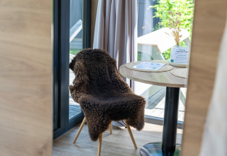 Coin accueillant dans une Tiny Home à Urban-Gardens Gent, Belgique, avec chaise, table et lumière naturelle.