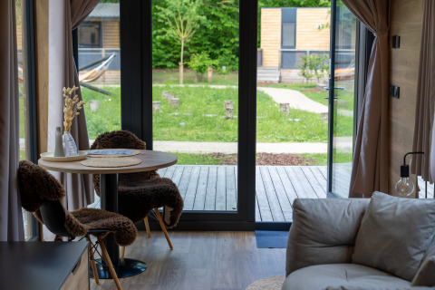 Vista interior de Tiny Home en Urban-Gardens Gent, Bélgica, con mesa de comedor y vista al jardín.