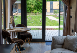 Vista interior de Tiny Home en Urban-Gardens Gent, Bélgica, con mesa de comedor y vista al jardín.