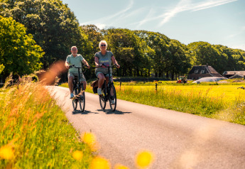 Zwei Personen fahren fröhlich mit dem Fahrrad auf einer Landstraße nahe einer Glamping-Unterkunft.